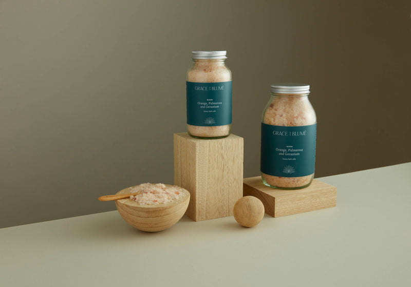 Our large and small BLOOM bath salts simply displayed on top of wooden oak blocks with some of the salts open and displayed with a small wooden spoon