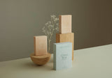 Two pale pink citrus rose salt bars sitting on wooden blocks with delicate dried white flowers in the background. The citrus rose box sits to the front showing the delicate rose embossing.